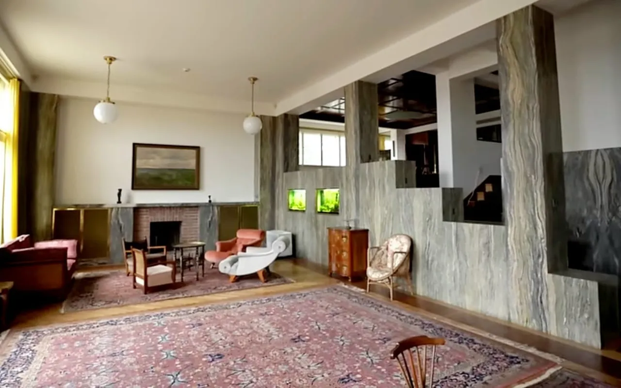 The living hall of Villa Müller with its green Cipollino marble wall, fireplace and rugs, the dining room opening above